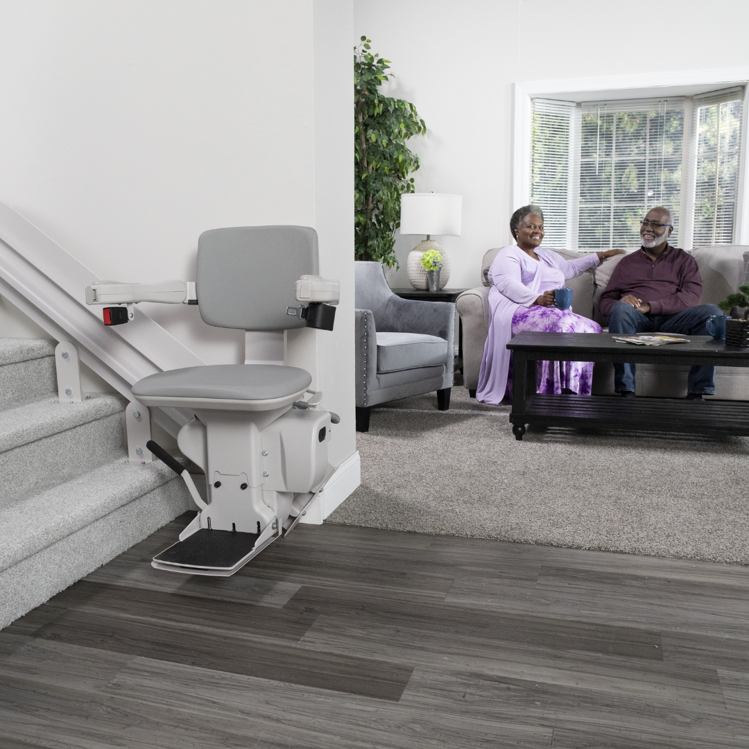 Man and woman seated on couch in background with stairlift in foreground - square image format