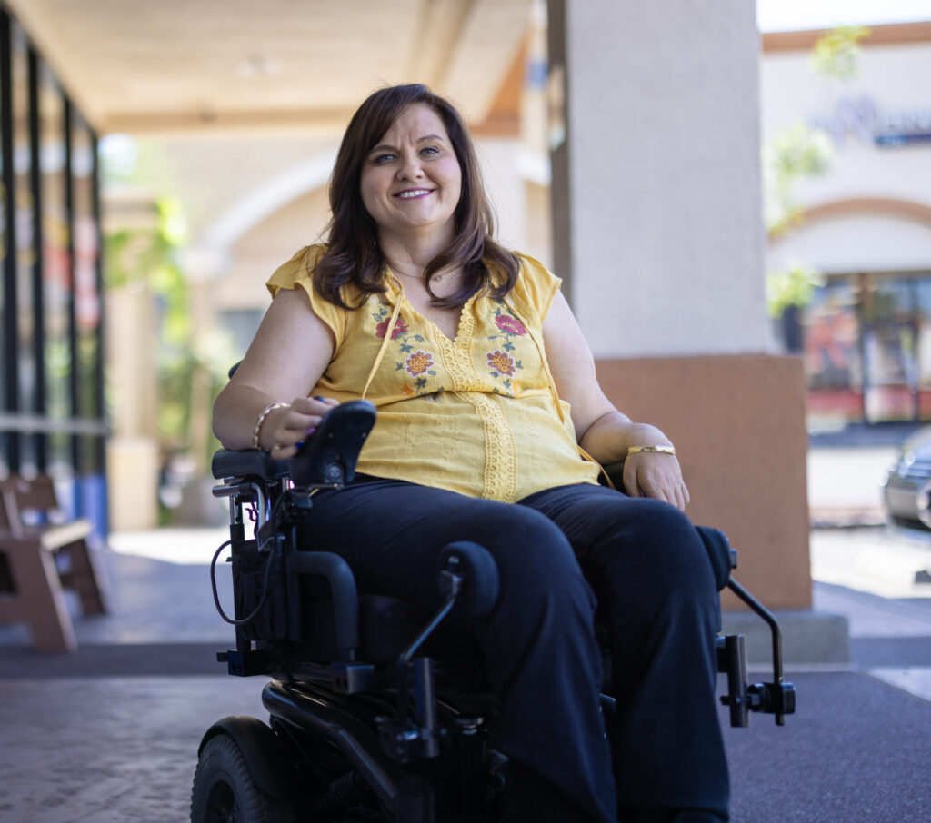 A young woman wearing a yellow tshirt in a power wheelchair.