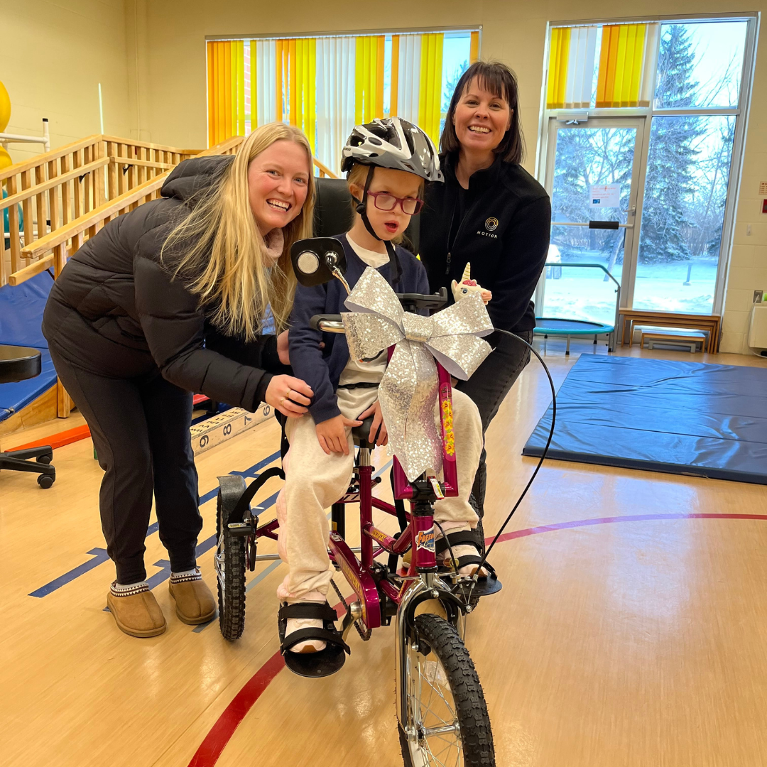 Anika in her new tricycle, her mother and a team member from Motion.